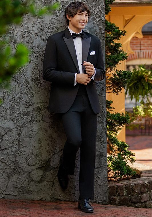 Young man in tuxedo leaning against wall